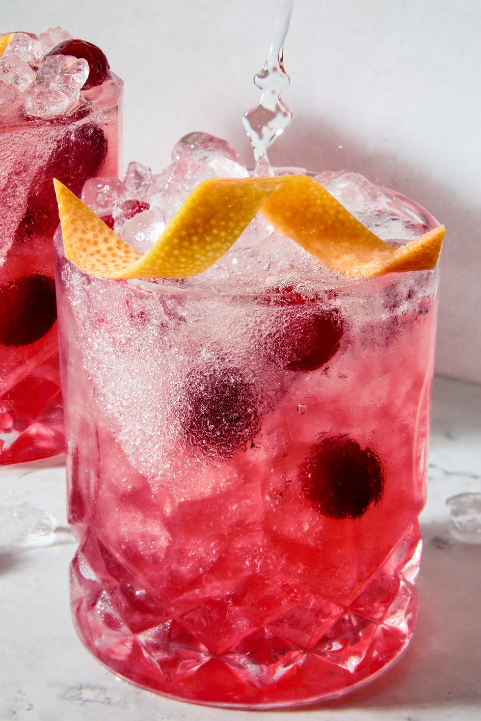 un petit verre bordé de sucre, rempli d'un cocktail de pamplemousse et de canneberges à la tequila, garni d'un zeste de pamplemousse et de canneberges fraîches