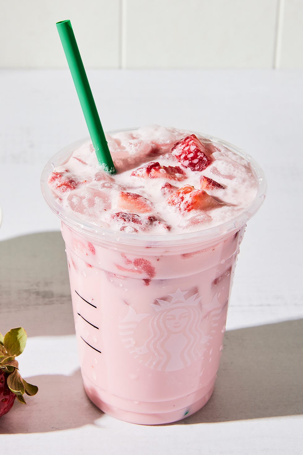 un grand verre avec une boisson crémeuse rose clair sur glace avec des tranches de fraises fraîches et une paille en verre