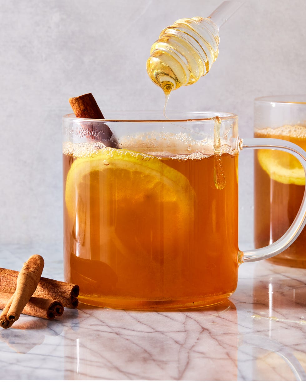 une tasse en verre remplie de whisky chaud, de miel et d'eau garnie de tranches de citron et de bâtons de cannelle