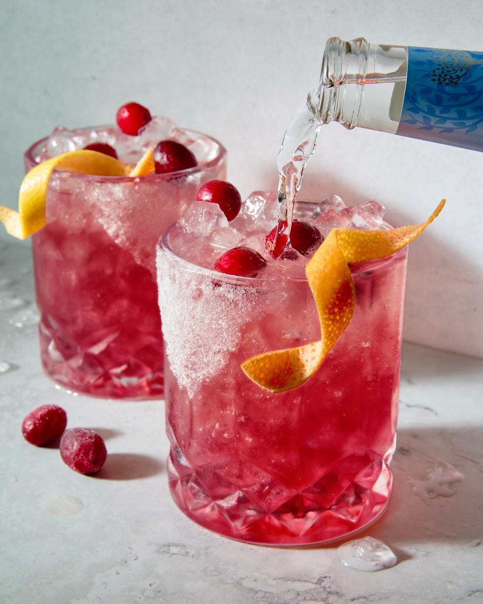 un petit verre bordé de sucre, rempli d'un cocktail de pamplemousse et de canneberges à la tequila, garni d'un zeste de pamplemousse et de canneberges fraîches