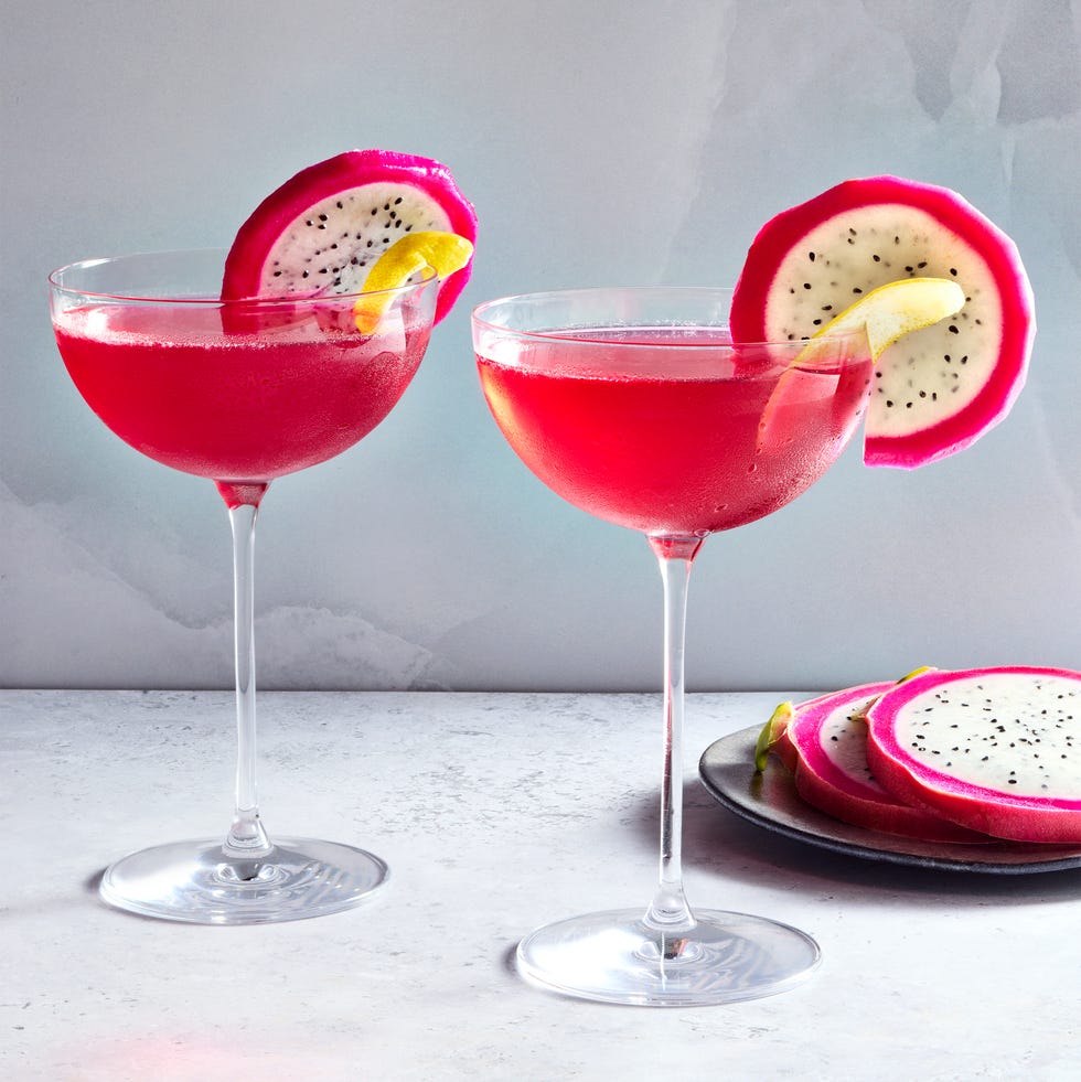 Dragon Fruit Drop Martini Deux verres de coupé remplis d'un cocktail à base de vodka rose vif et garni d'une tranche de fruits de dragon et d'une touche de citron