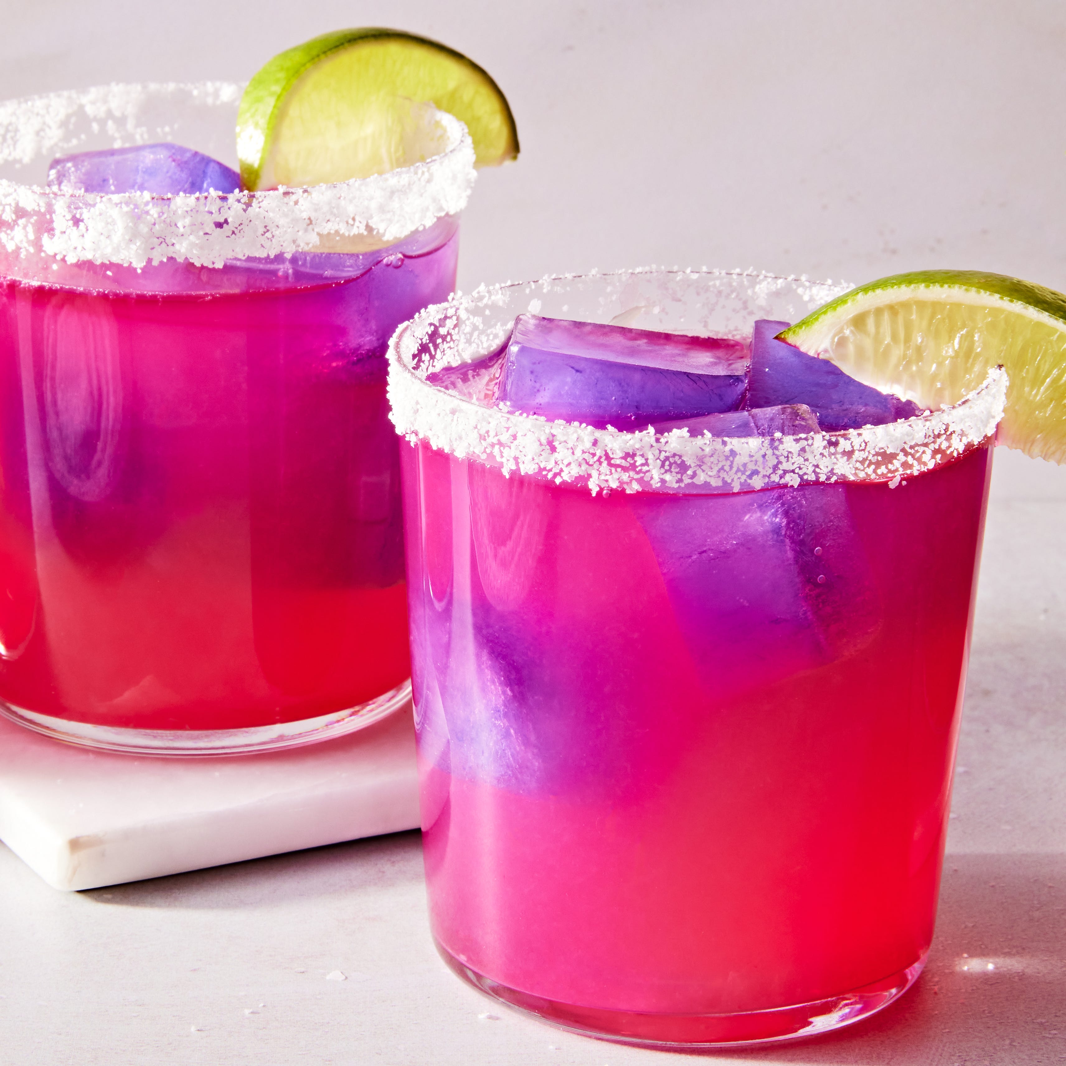 Margaritas aux couleurs changeantes margarita rose avec un glaçon violet avec un bord de sel et un quartier de citron vert