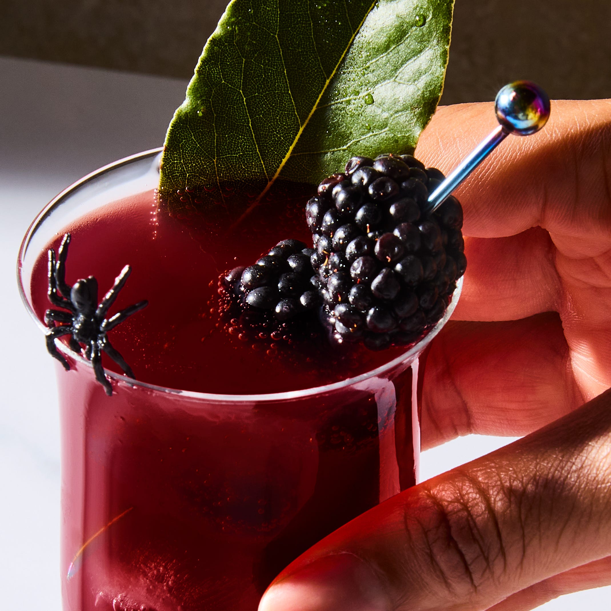 Cocktail de la veuve noire cocktail rouge foncé garni de mûres et de feuilles de laurier