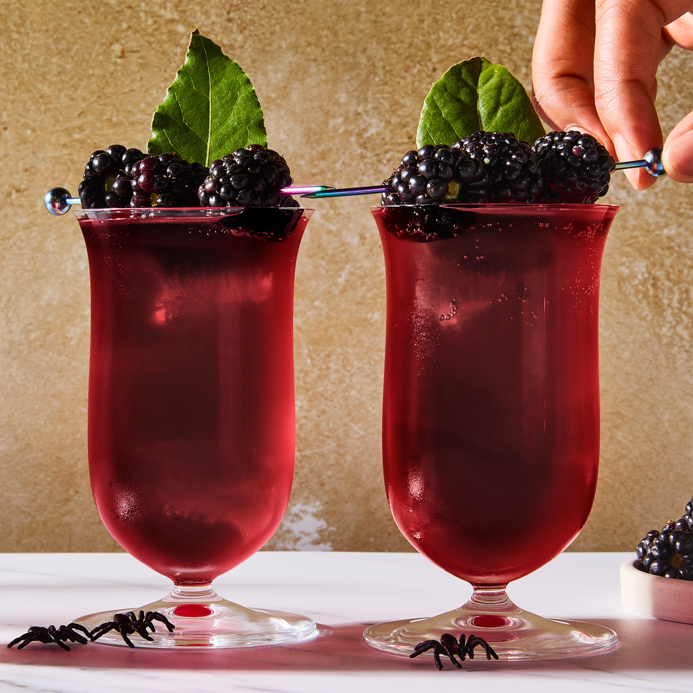 Cocktail de la veuve noire cocktail rouge foncé garni de mûres et de feuilles de laurier