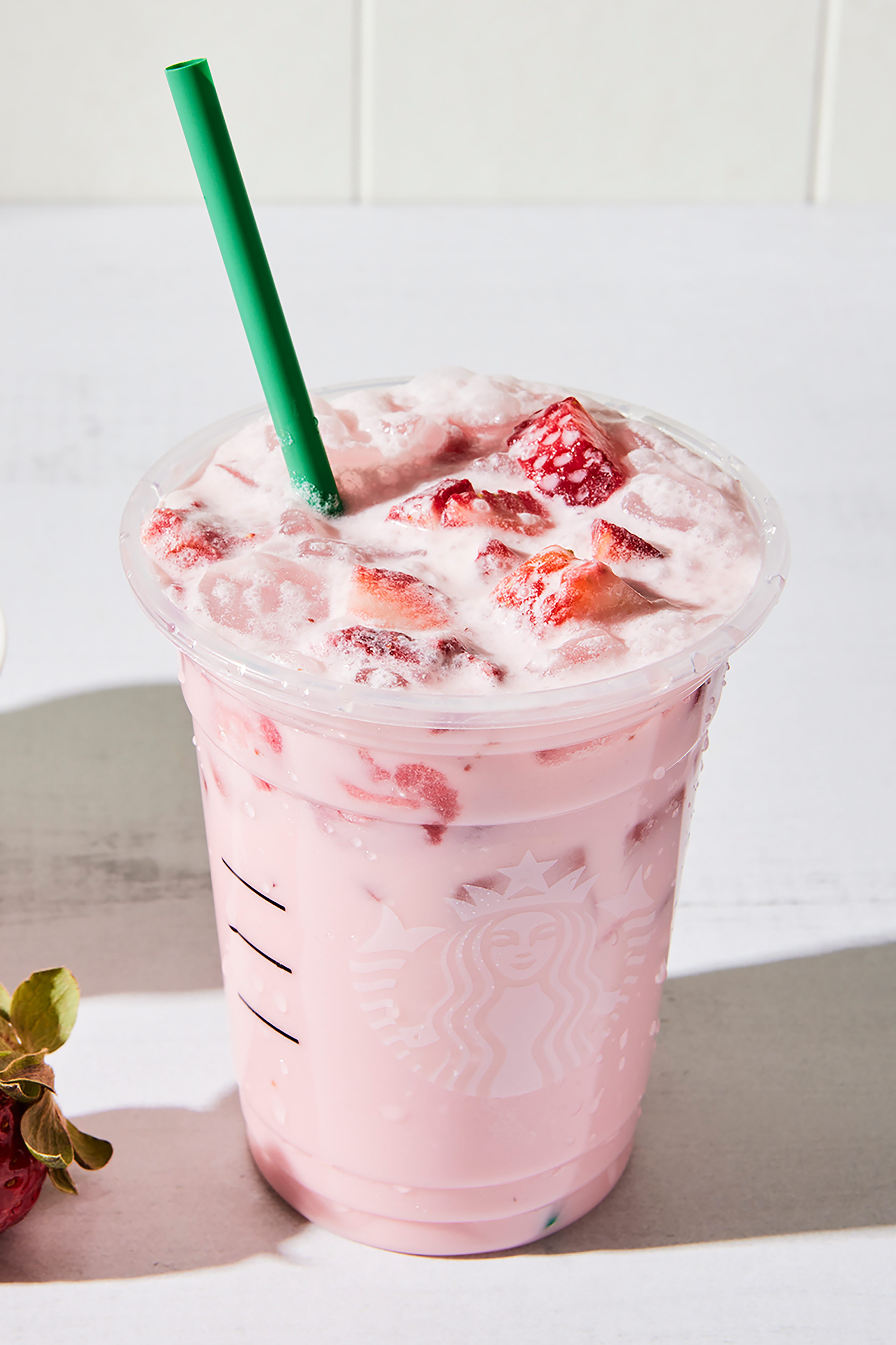 un grand verre avec une boisson crémeuse rose clair sur glace avec des tranches de fraises fraîches et une paille en verre