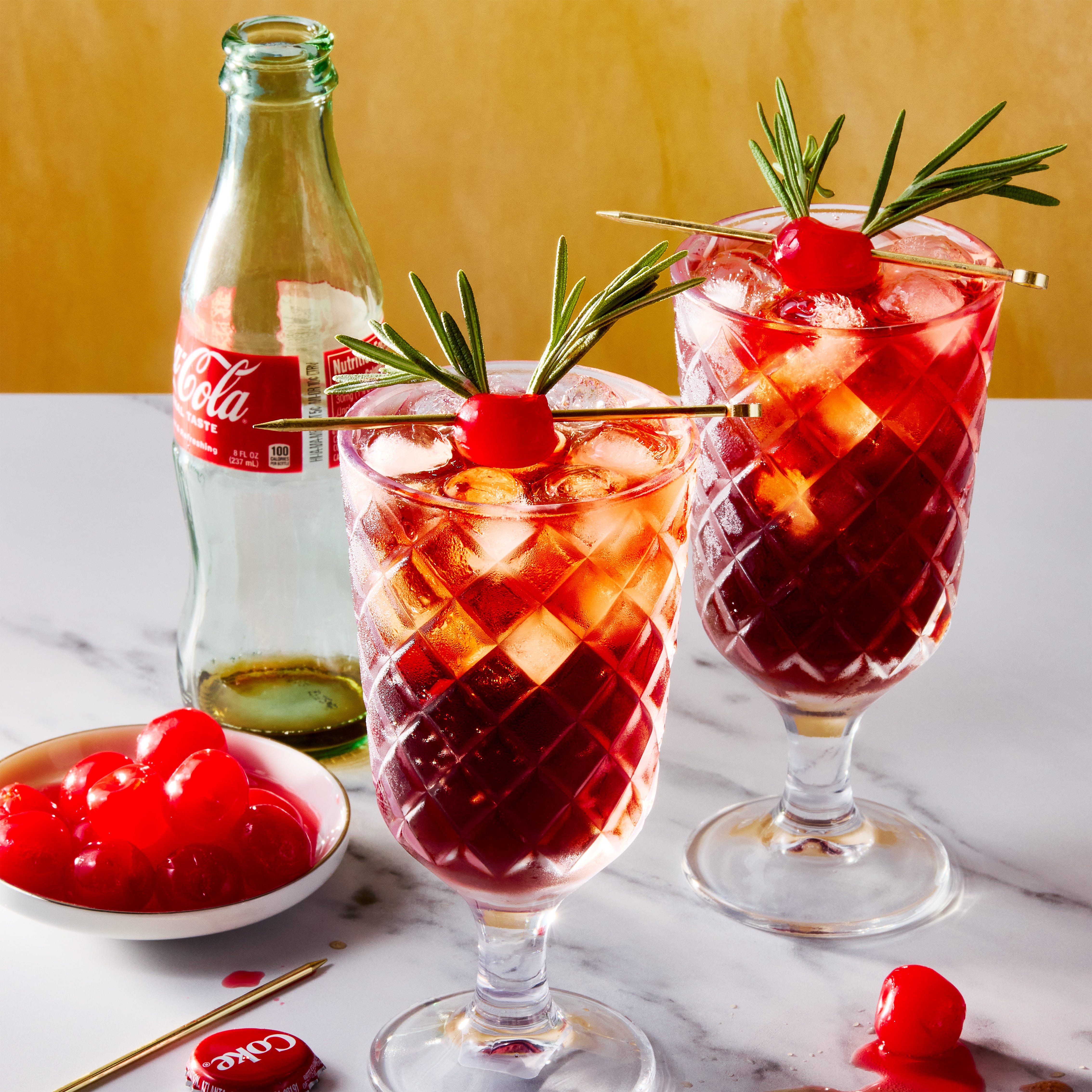 deux verres remplis de glace, de rhum, de jus de cerise et de cola, garnis d'une cerise au marasquin décorée de deux brins de romarin